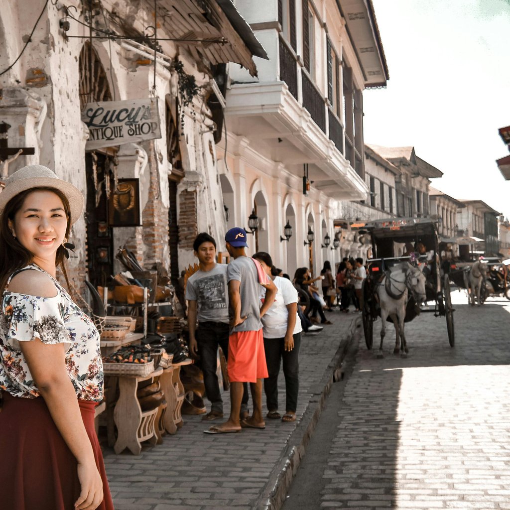 A woman poses on Calle Crisologo in Vigan City, showcasing colonial architecture and bustling street life.