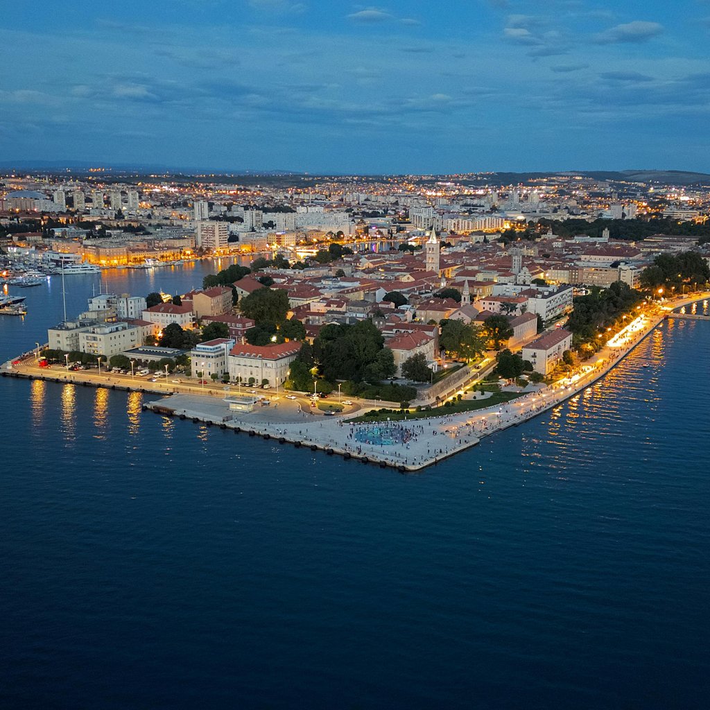 Stunning aerial view of Zadar's illuminated coast at twilight, showing the vibrant cityscape.