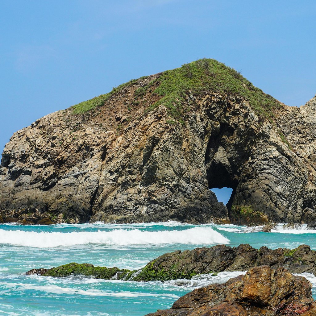 Majestic rock formation with ocean waves at Zipolite Beach, Oaxaca, Mexico, perfect coastal scenery.